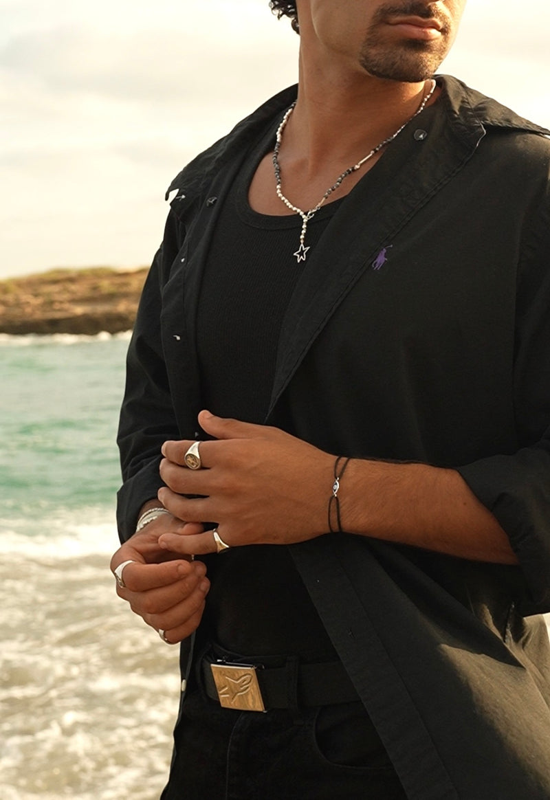 Man wearing a black outfit with jewelry by the water