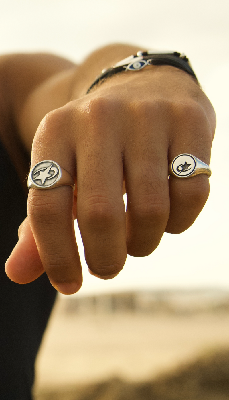 Hand wearing two rings with visible logos against a blurred background