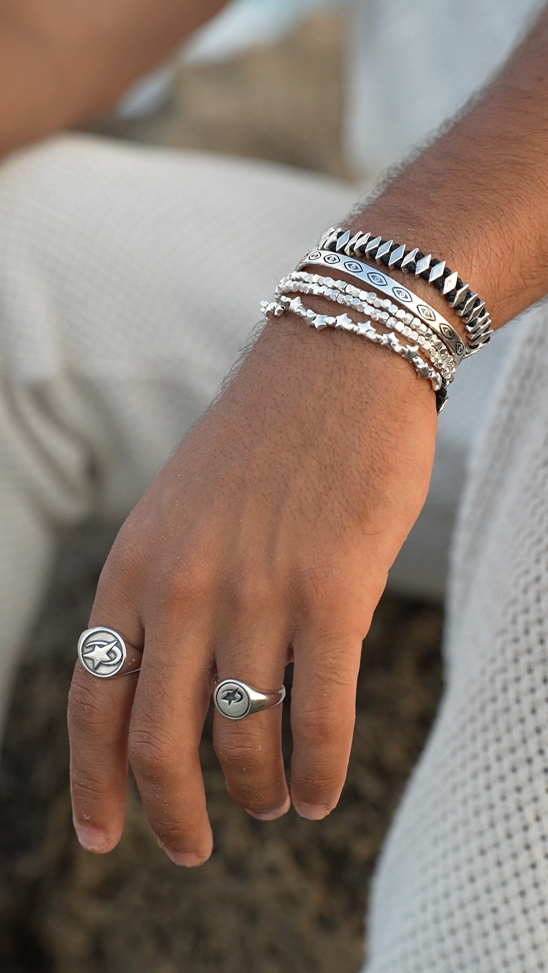 Hand wearing multiple silver rings and bracelets with a blurred background