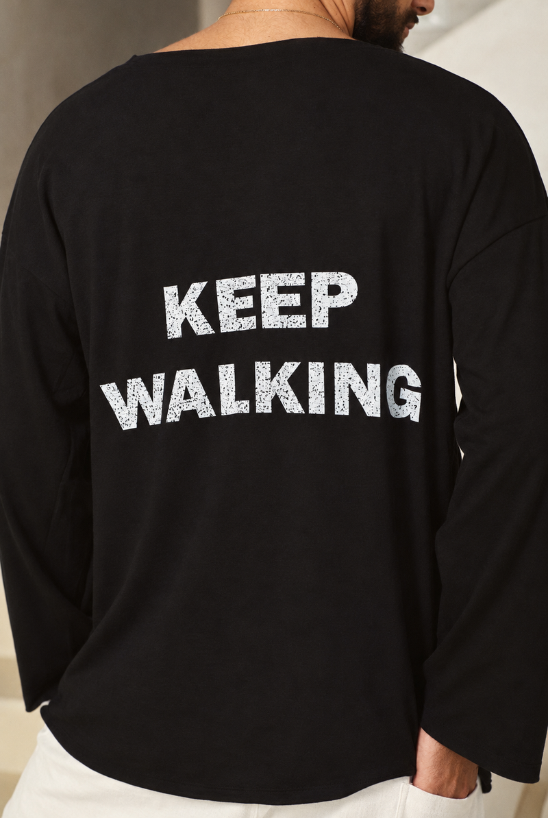 תקריב הכיתוב הלבן KEEP WALKING בגב חולצה שחורה